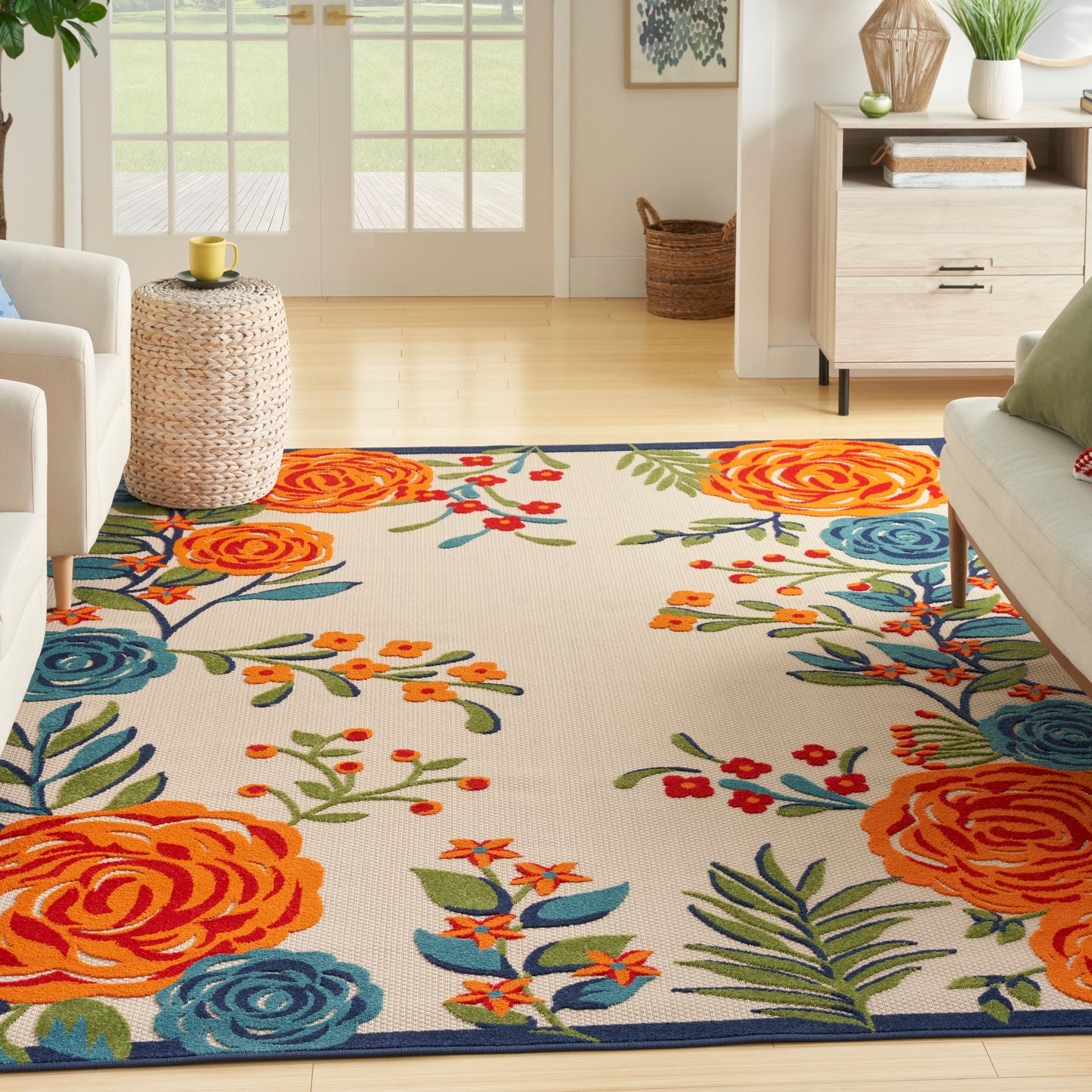 Bright living room with a vivid floral rug in orange, blue, and green, cream sofas, and a wicker side table.