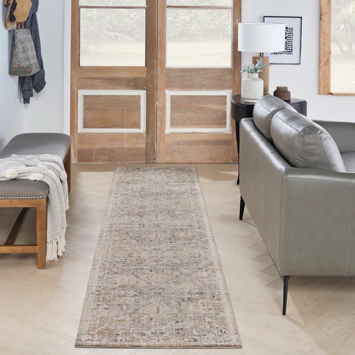 Neutral beige runner rug runs down a light wood floor in a contemporary living room with a gray leather sofa and wooden doors.