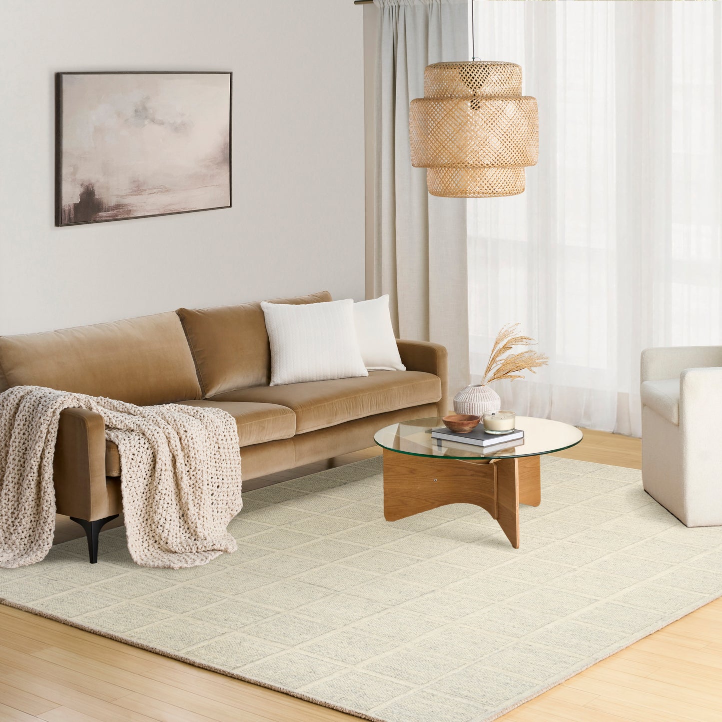 Beige sofa with white cushions and knit throw, round glass coffee table on a light geometric rug in a bright living room