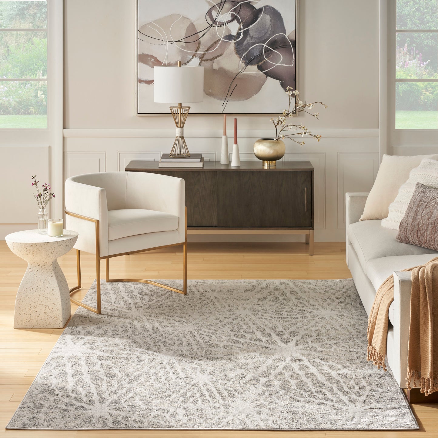 Neutral living room with a gray geometric patterned rug, white upholstered chair, wood console, and abstract wall art.