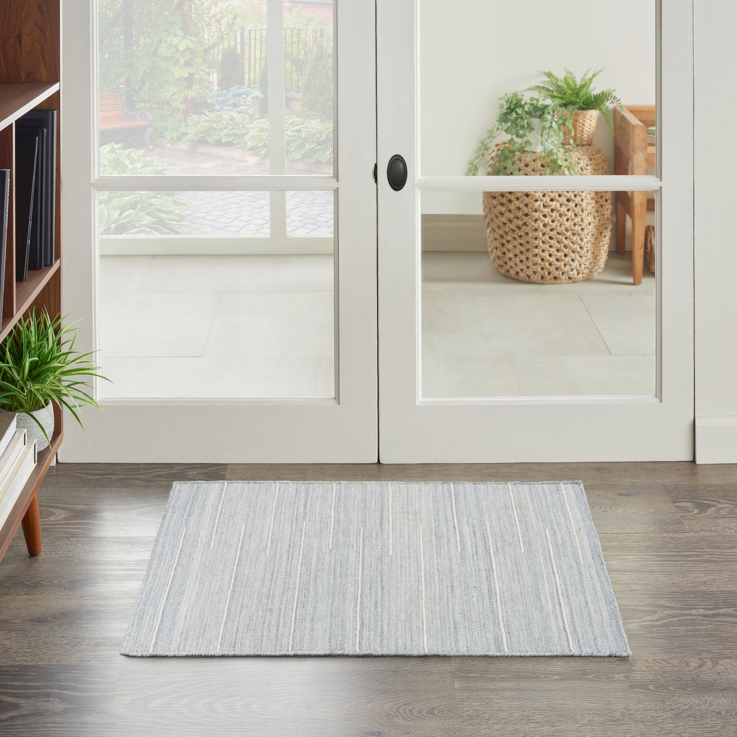 Light gray-blue striped rug on dark wood floor by glass doors; indoor plant and woven basket visible outside.