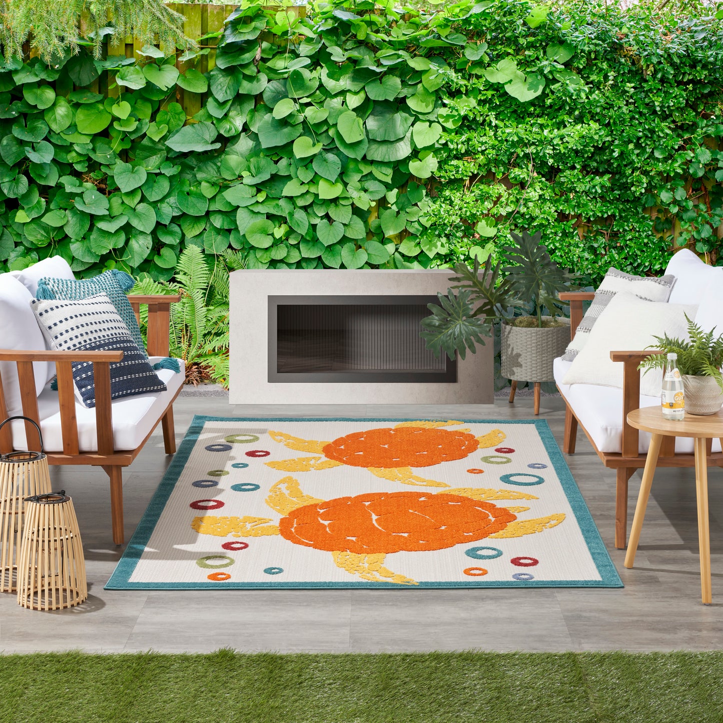 Outdoor seating area with white cushions, a rectangular fireplace, lush green wall, and a rug with orange lobsters.