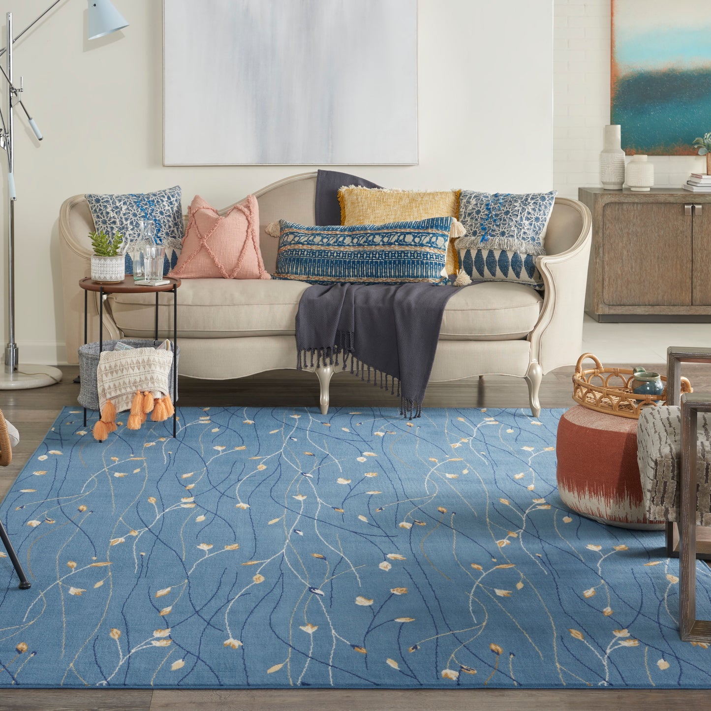 Cozy living room with beige tufted sofa, blue patterned rug, and colorful throw pillows; navy fringed blanket.