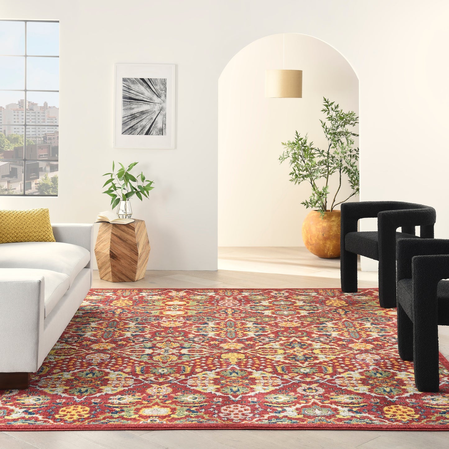 Bright living room with a red patterned rug, white sofa, yellow pillow, black arched chairs, and potted plants.