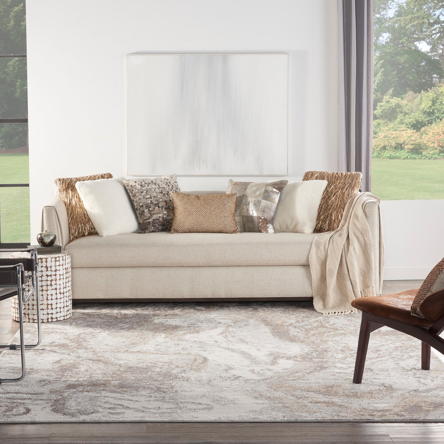 Beige sofa with diverse textured pillows, draped throw, woven side table, gray abstract rug in bright living room
