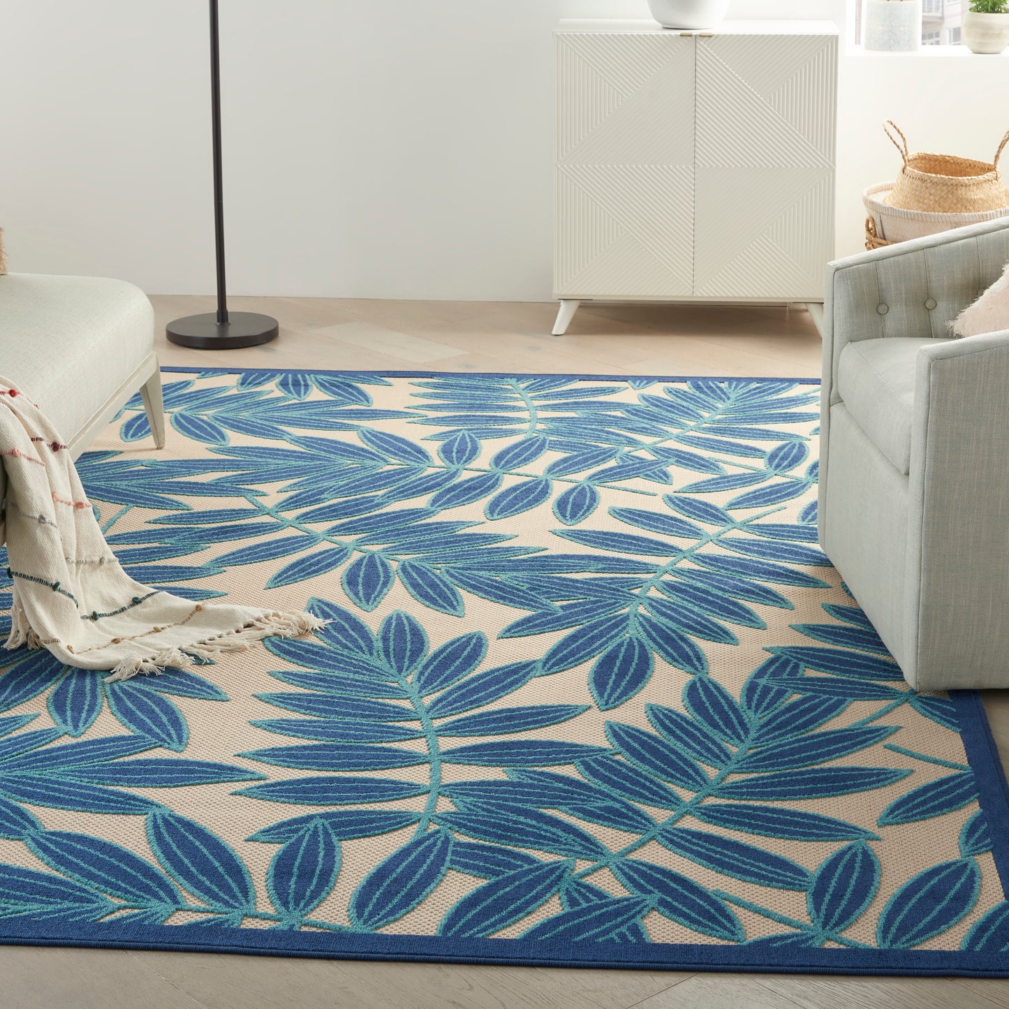 Blue palm leaf-pattern area rug in a beige living room with a gray sofa and white cabinet.