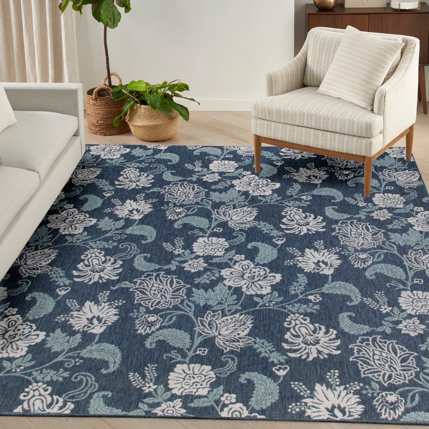 Blue floral area rug with white blossoms in a cozy living room, beige armchairs and potted plants.