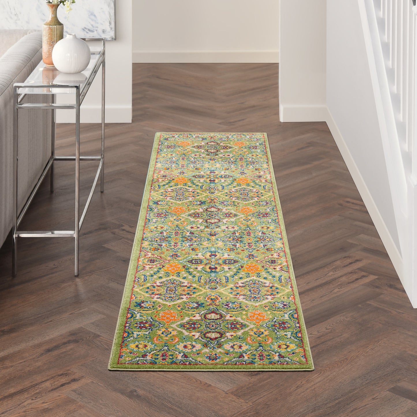 Vibrant oriental-style hallway runner rug with lime-green border on dark wood herringbone floor by a metal console table.
