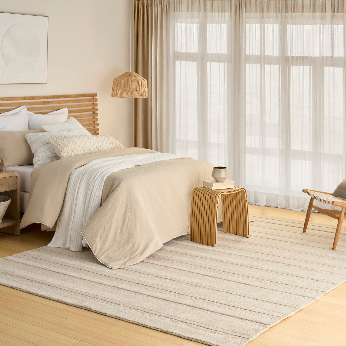 Neutral beige bedroom with wooden bed frame, cream bedding, woven lamp, striped rug, bamboo side table, sheer curtains.