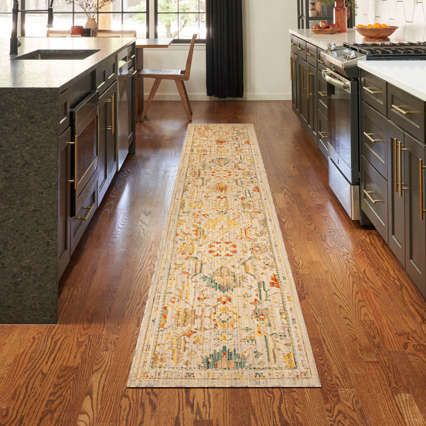 Oriental-style rug runner with cream base and orange/blue accents on hardwood kitchen floor between dark cabinets and island.