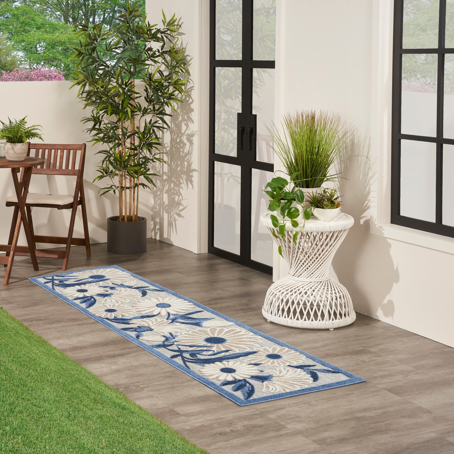 Blue floral runner rug with beige background on wood flooring in a sunroom with potted plants and black-framed glass doors.