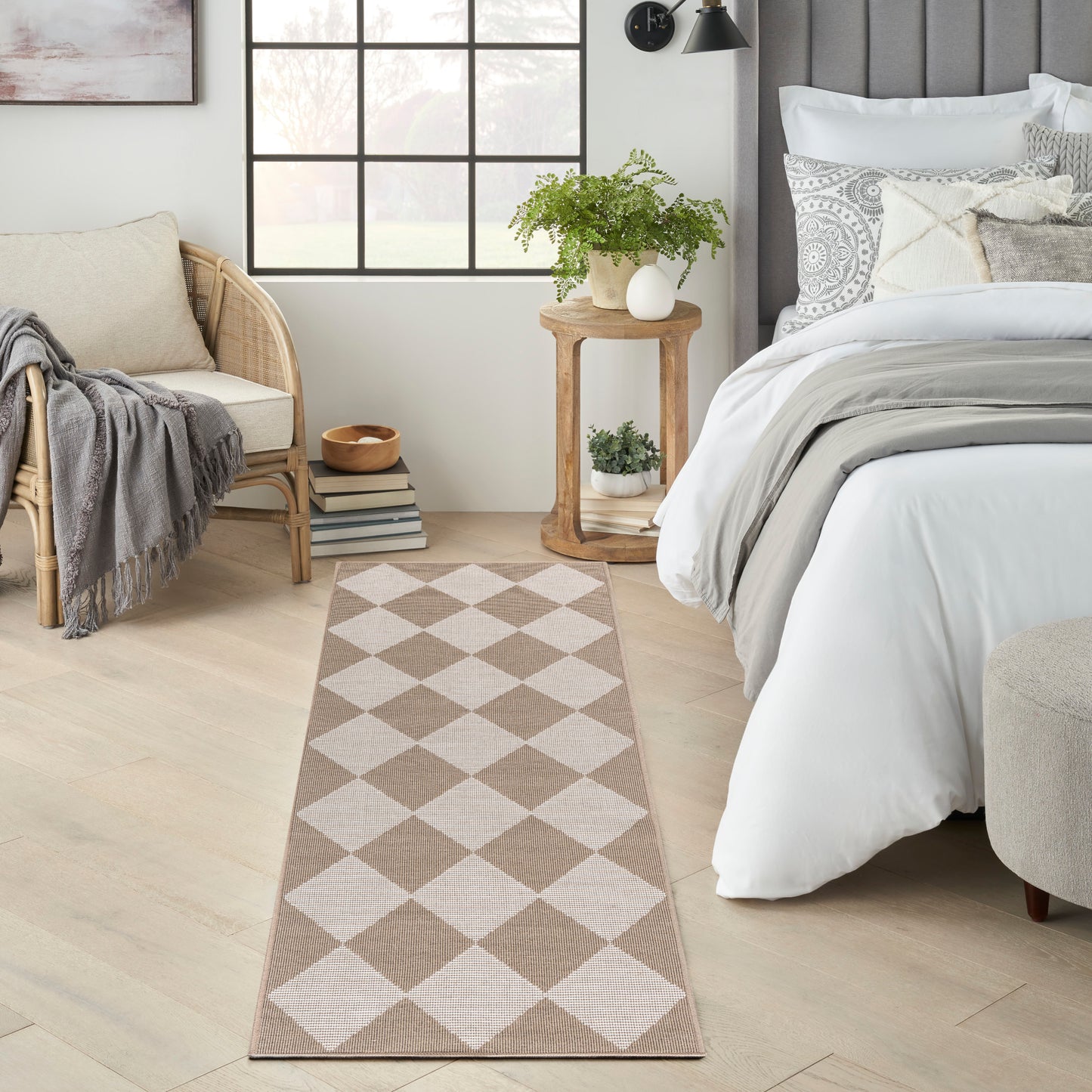 Beige and white diamond-pattern runner rug in a bright bedroom with a bed, wicker chair, and potted plants.