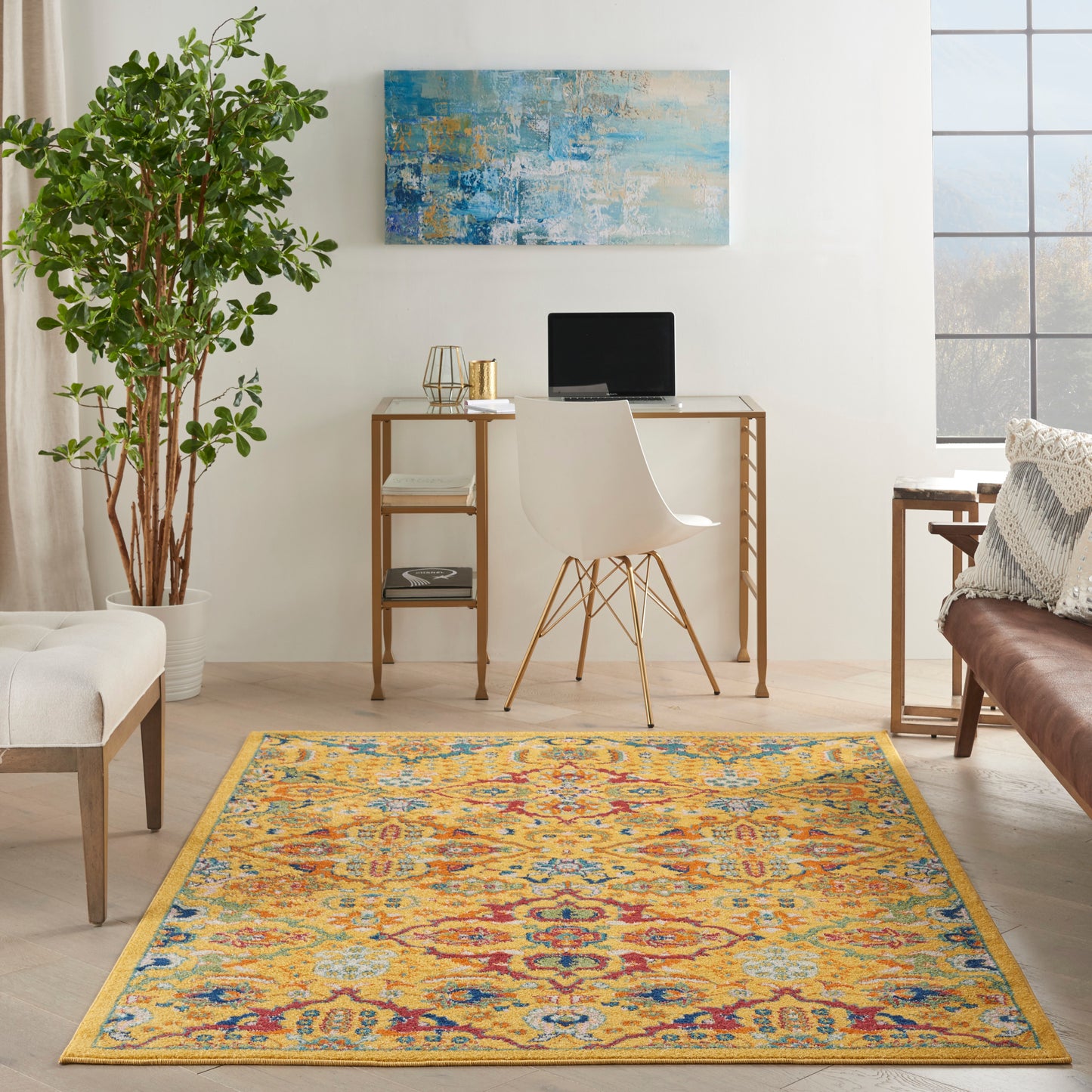 Colorful boho area rug with yellow border on light wood floor; white desk chair, desk, laptop, plant, blue art.