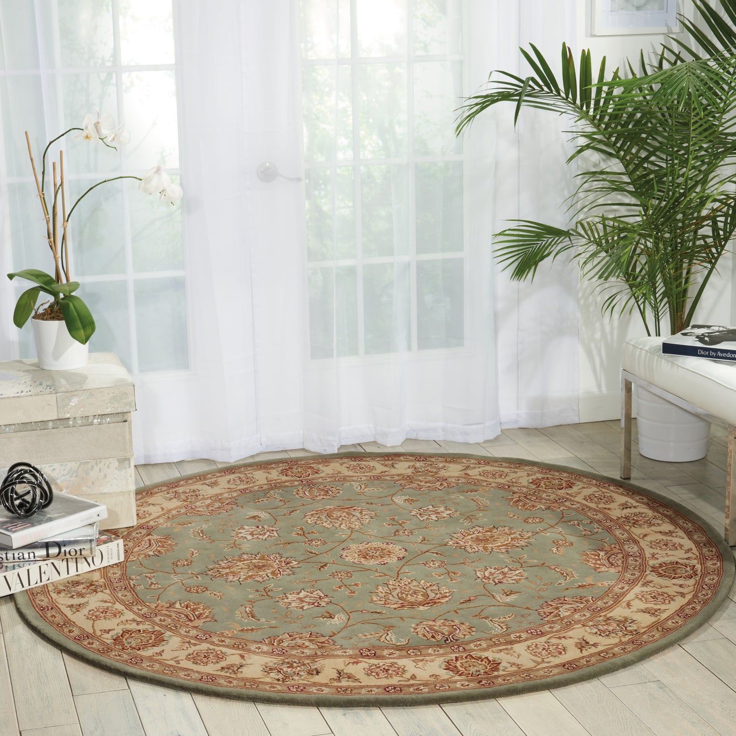 Round oriental rug with teal center and ornate red-brown border, in a bright living room with plants.