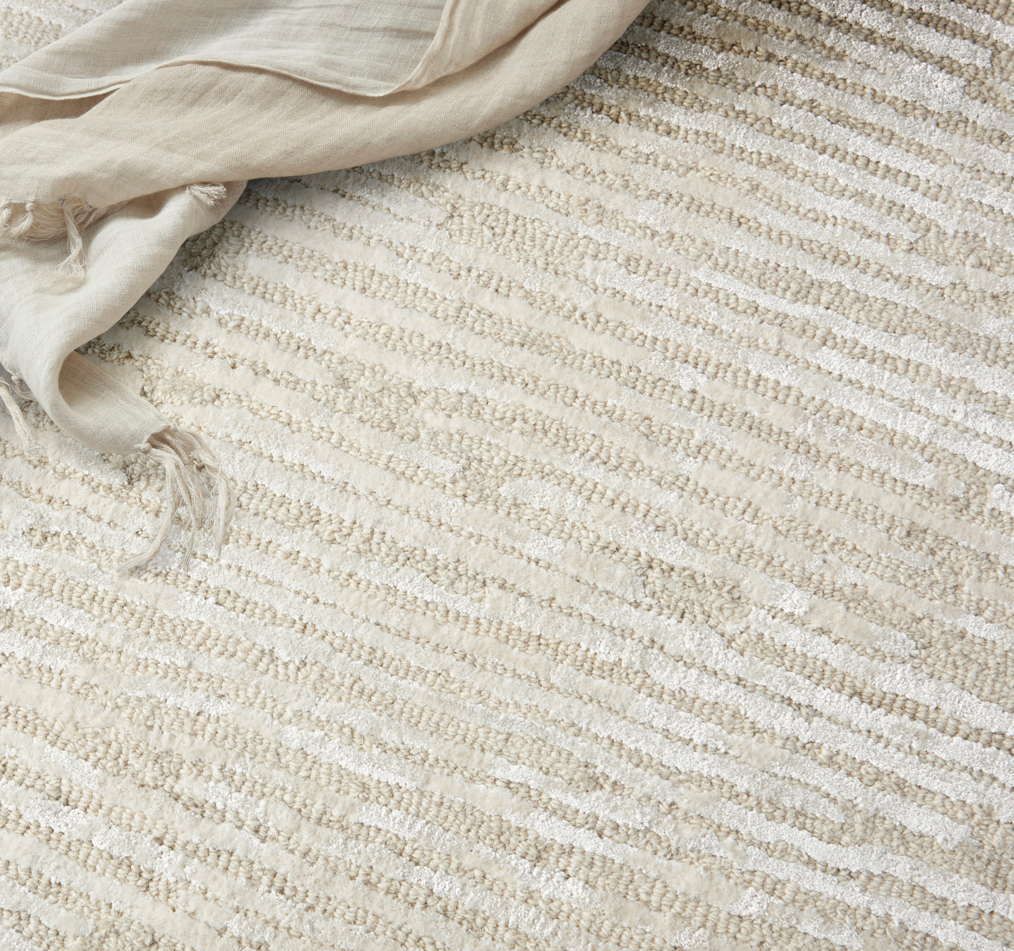 Cream and beige striped woven rug with soft, textured surface; light linen throw draped at corner.