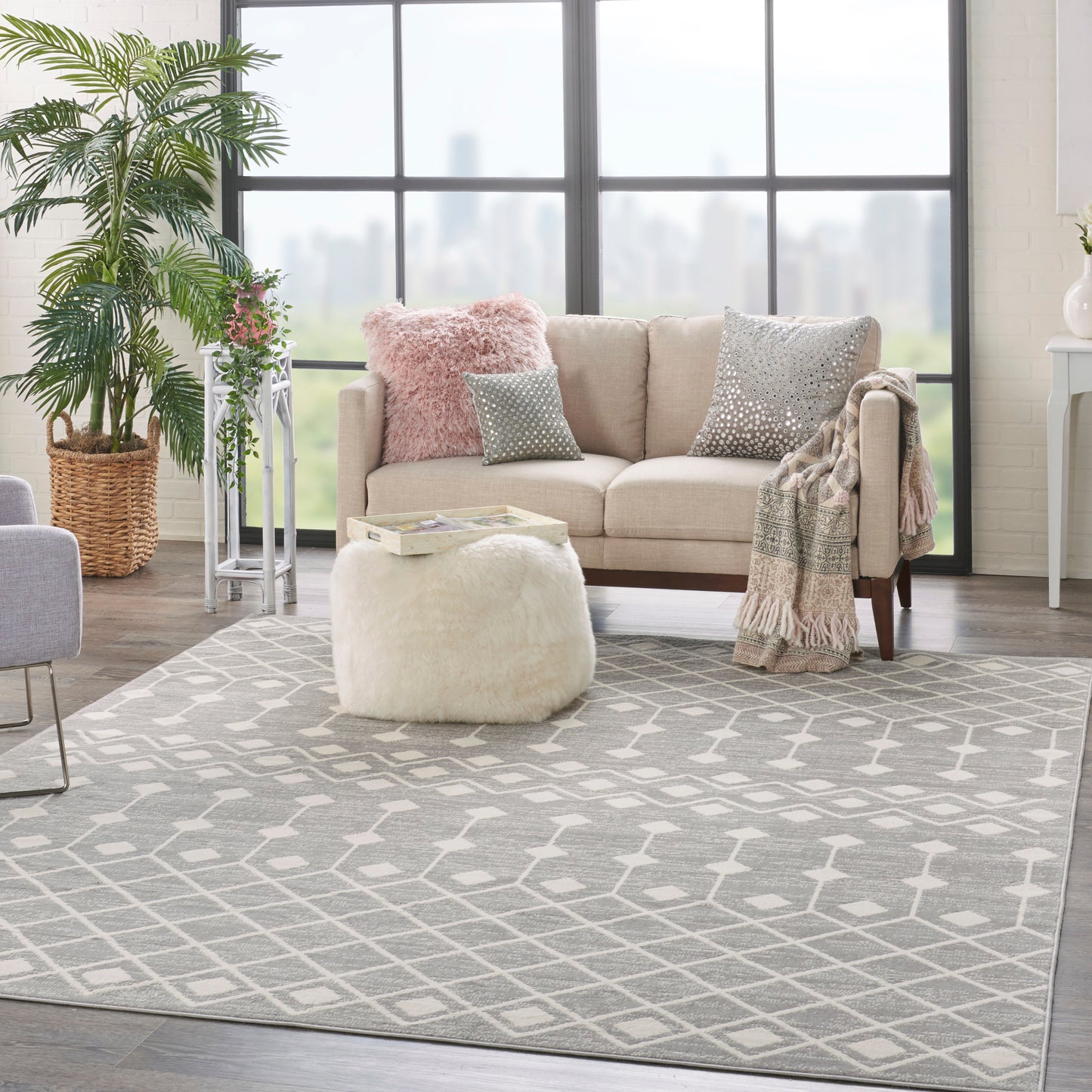 Beige fabric sofa with pink and gray cushions, cream plush ottoman, woven plant basket, and gray geometric rug.