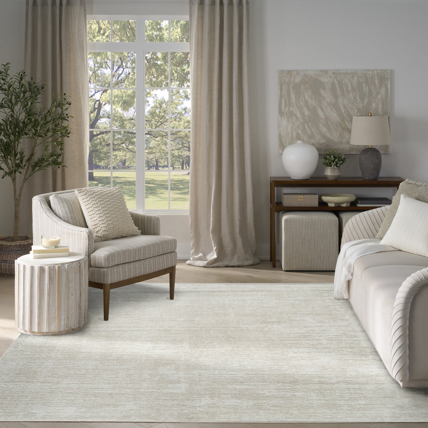 Neutral living room with a light beige area rug, cream sofa, striped armchair, and wooden console under a large window.