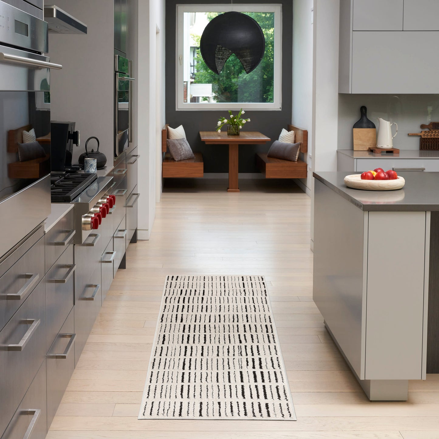 Contemporary kitchen with stainless steel appliances, light wood floors, gray island, white cabinets, and a striped runner rug.