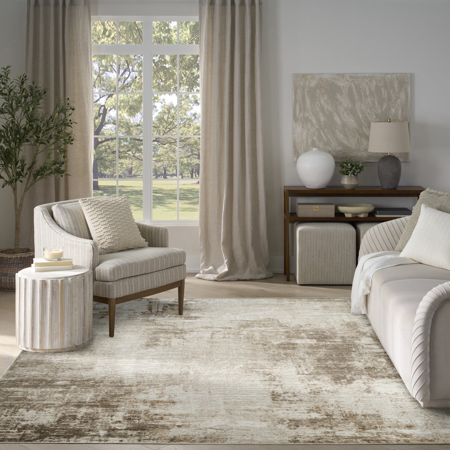 Neutral living room with beige curtains, cream sofa and striped armchair, round ribbed side table, large window view and rug.