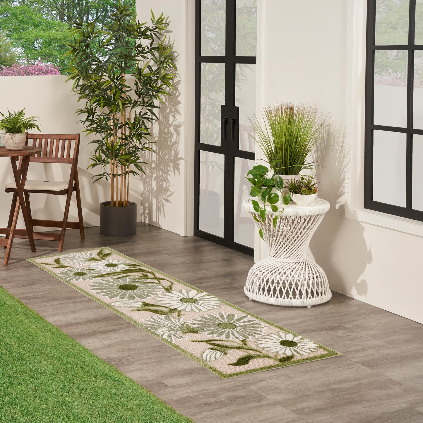 Long beige-green floral runner rug with white daisies; flat-woven, placed beside glass doors with potted plants.