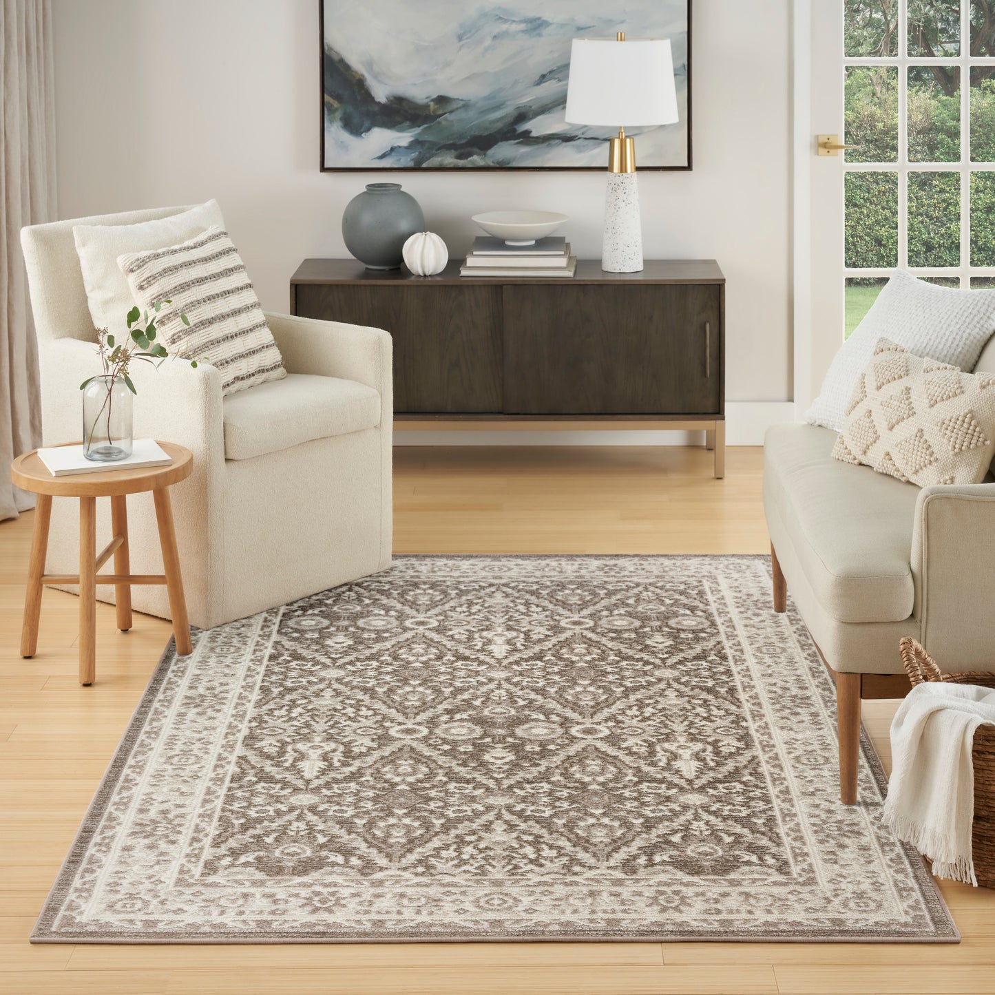 Neutral living room with taupe-ivory patterned area rug, cream sofa and armchair, wooden side table, and dark wood console.