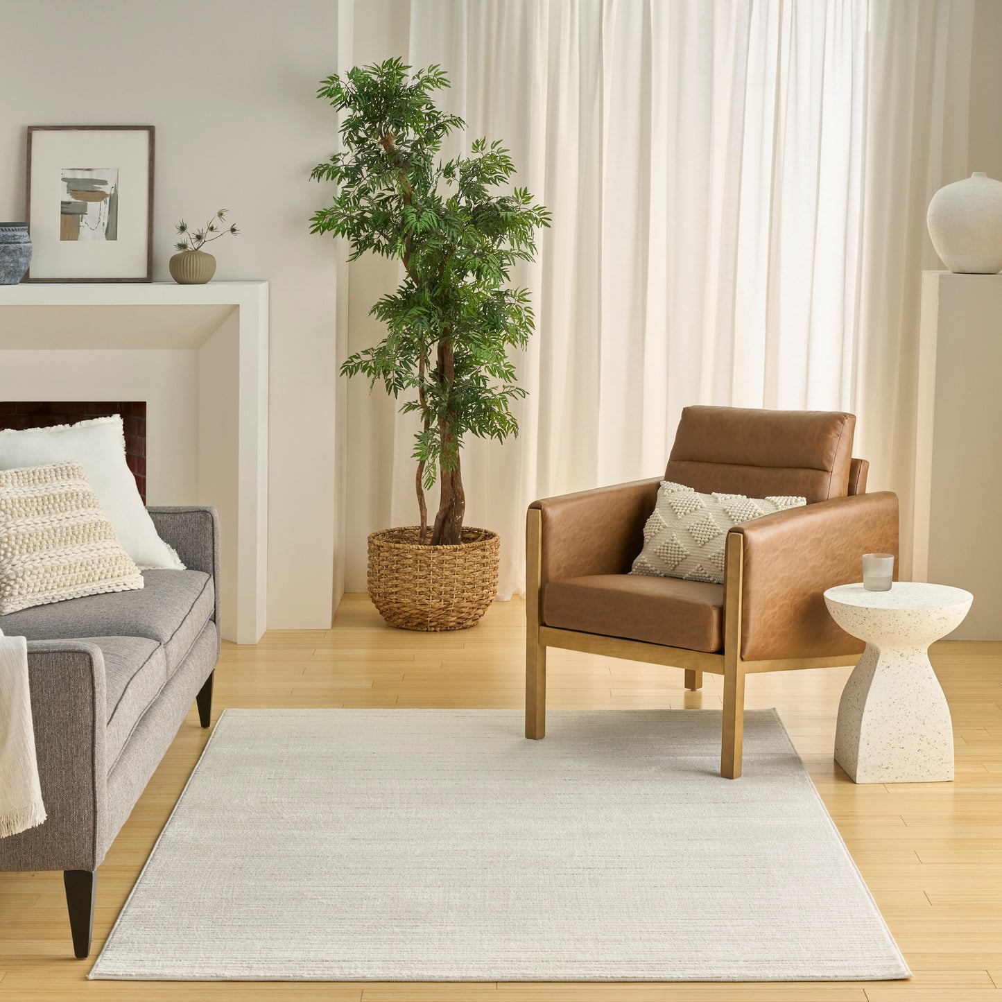 Modern living room with grey fabric sofa, brown leather armchair, cream rug, tall potted plant, light wood floors.