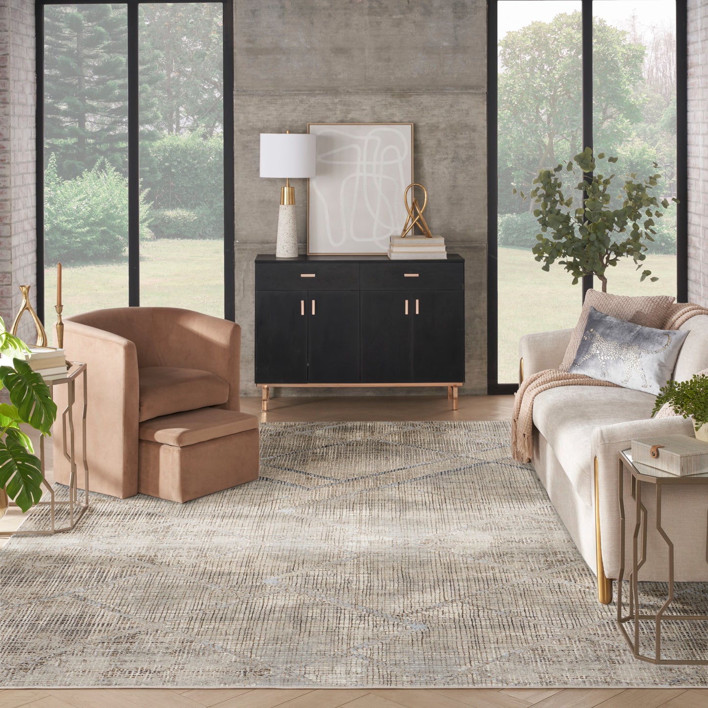 Contemporary living room with a black mid-century sideboard, tan armchair, beige sofa, light patterned rug, gold accents and large windows.