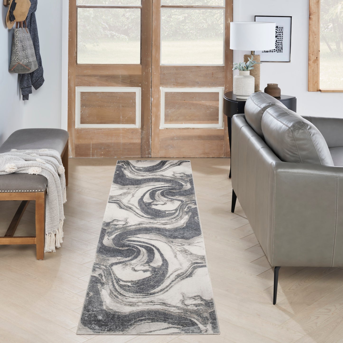 Gray & white marble swirl runner rug on light wood floor in a living room with sofa, bench, coat rack and entry doors.