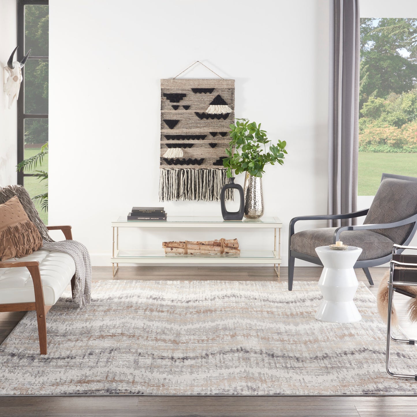Bright modern living room with a large rug (9' x 12'), white walls, boho wall hanging, glass console, log accent, potted plant, sofa and chair.