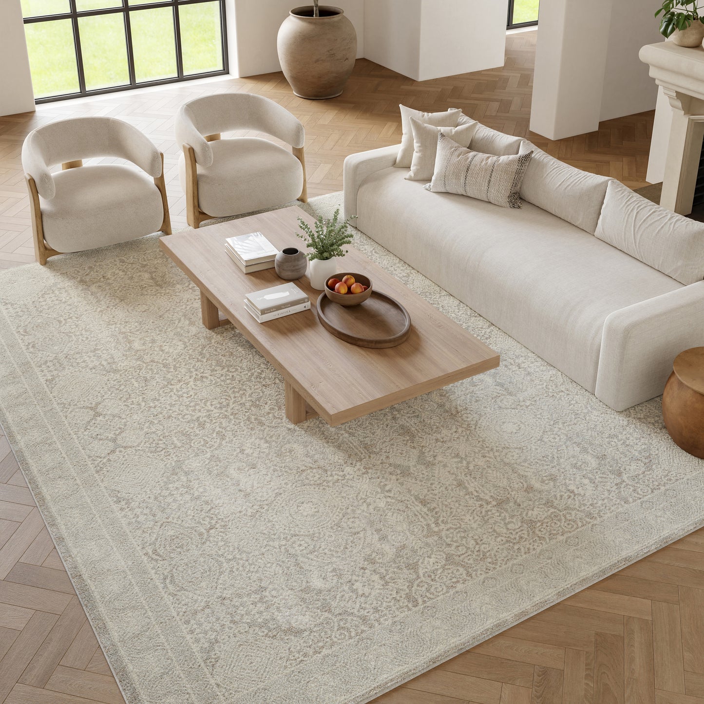 Beige patterned rug in a neutral living room with a cream sofa, two curved beige armchairs, and a light wood coffee table.