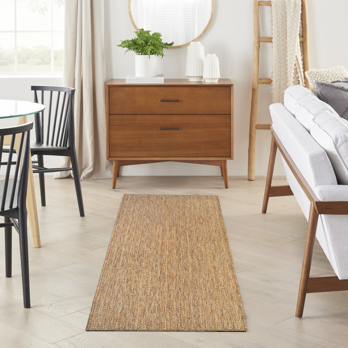 Natural jute runner rug in a bright living room with a mid-century walnut dresser, black dining chairs, and a white sofa.