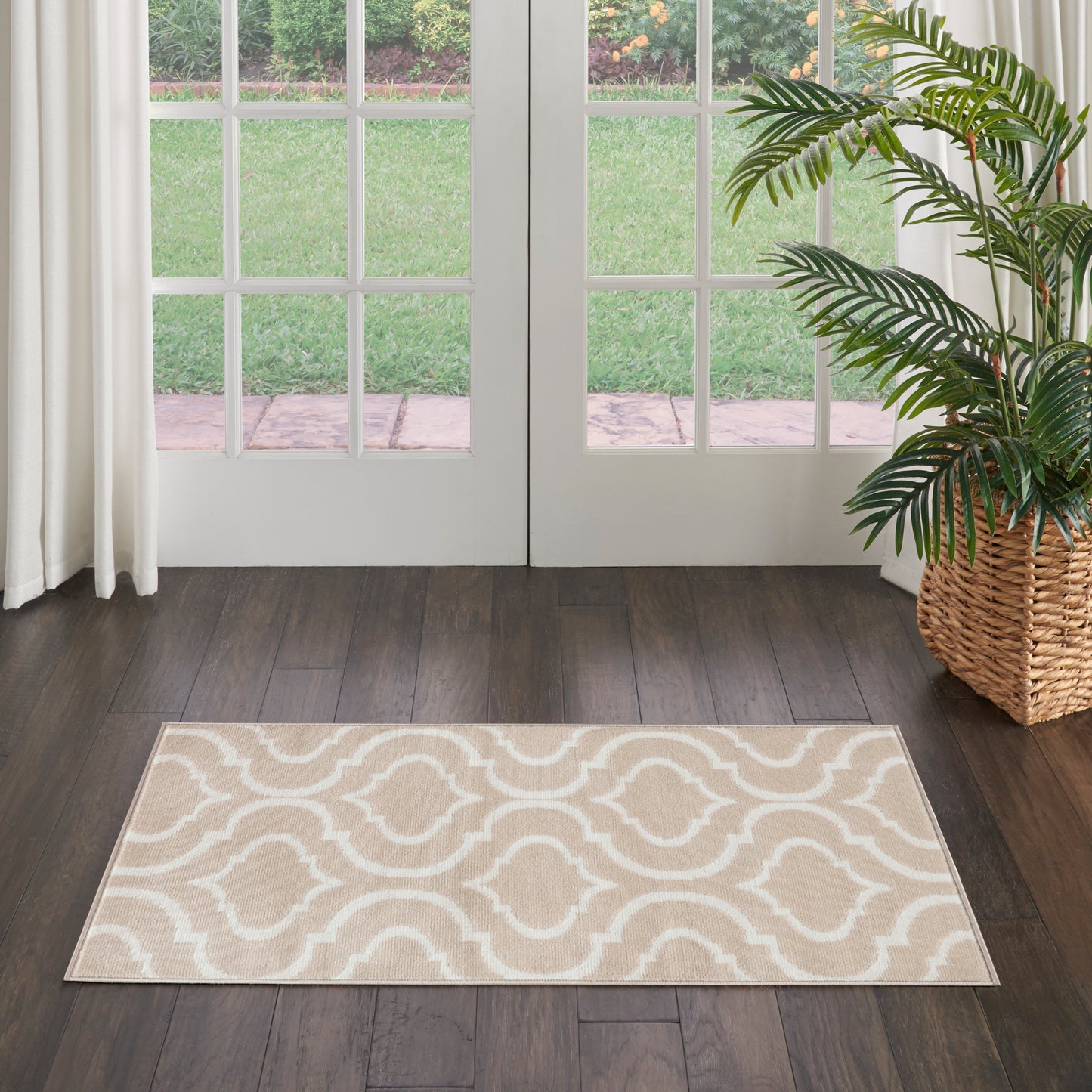 Beige and white geometric trellis area rug on dark wood floor beside glass French doors and a potted palm in a wicker planter