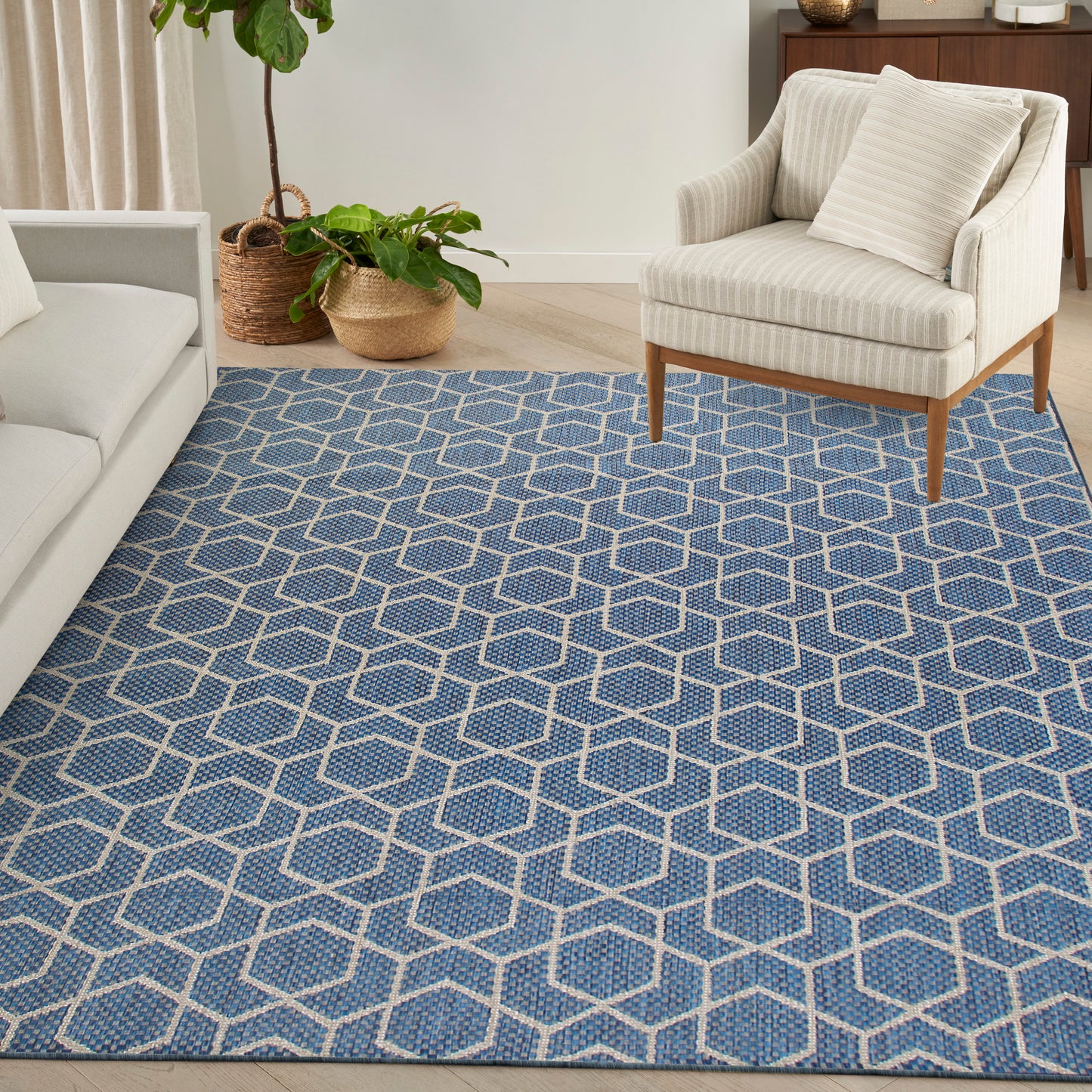Blue geometric hexagon-pattern rug with cream lines, woven texture in a cozy living room beside beige armchair and sofa.