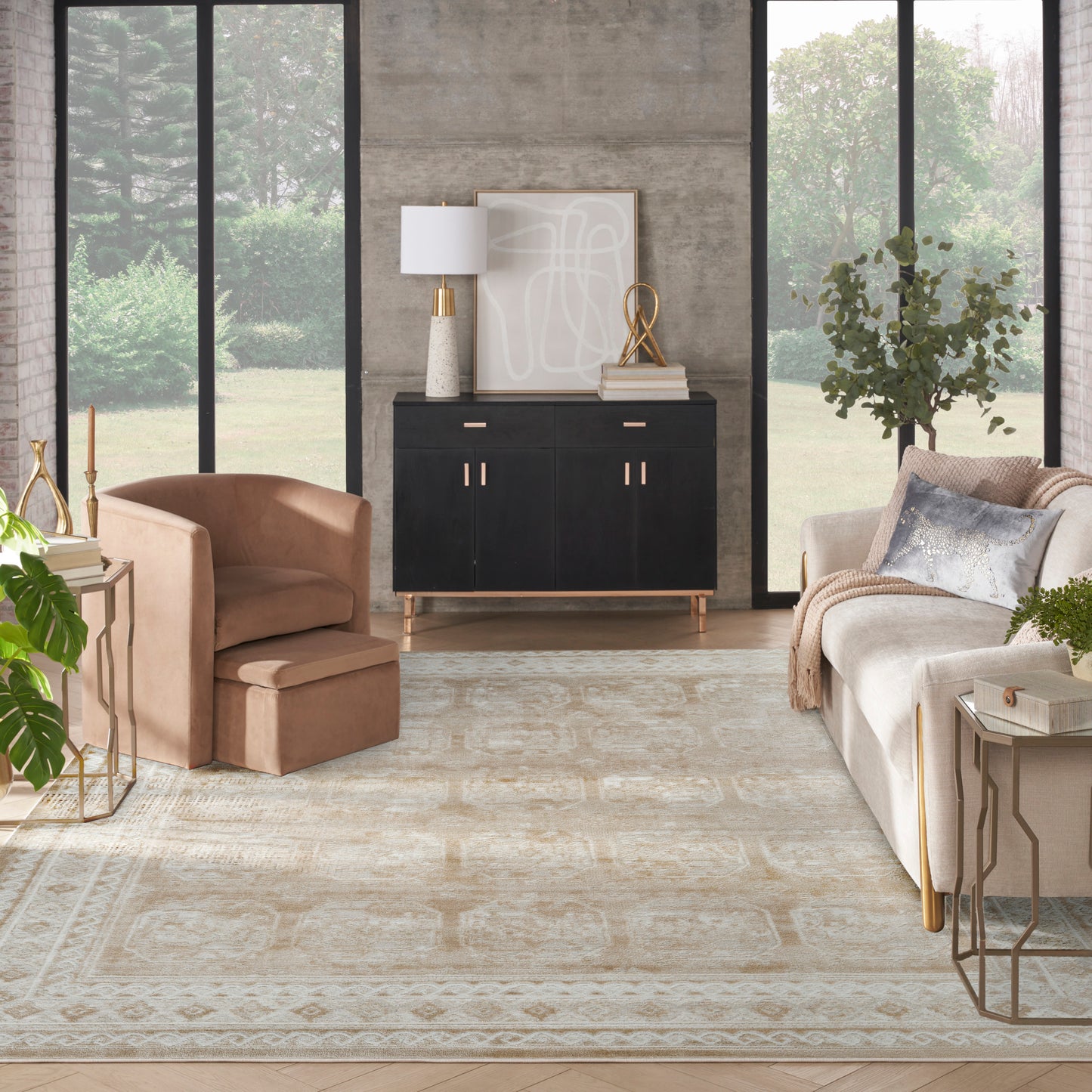 Modern living room with large windows, beige sofa, blush armchair, black cabinet with gold handles, light rug, gold accents.