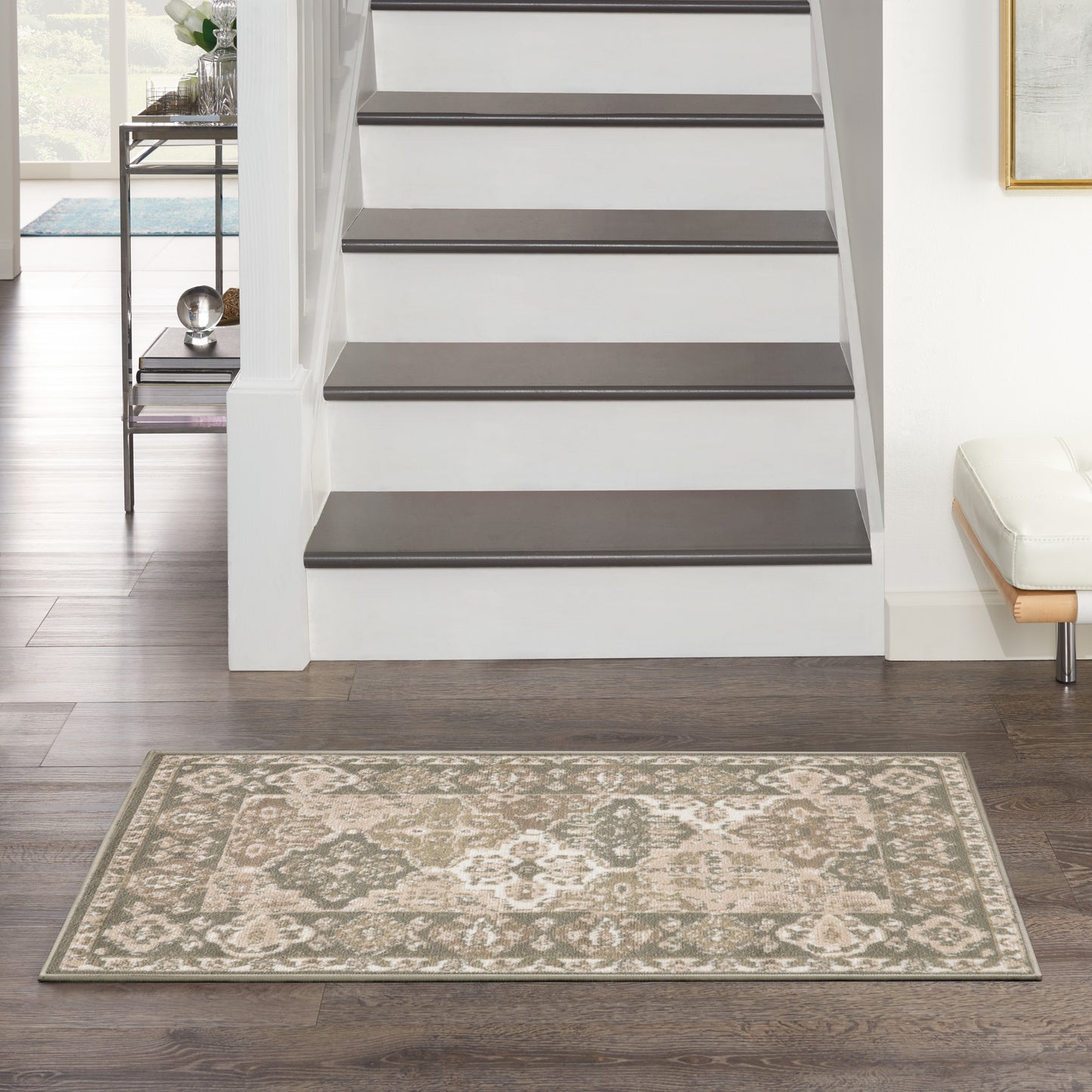 Rectangular beige-taupe ornate damask area rug on dark hardwood floor beside a white staircase.