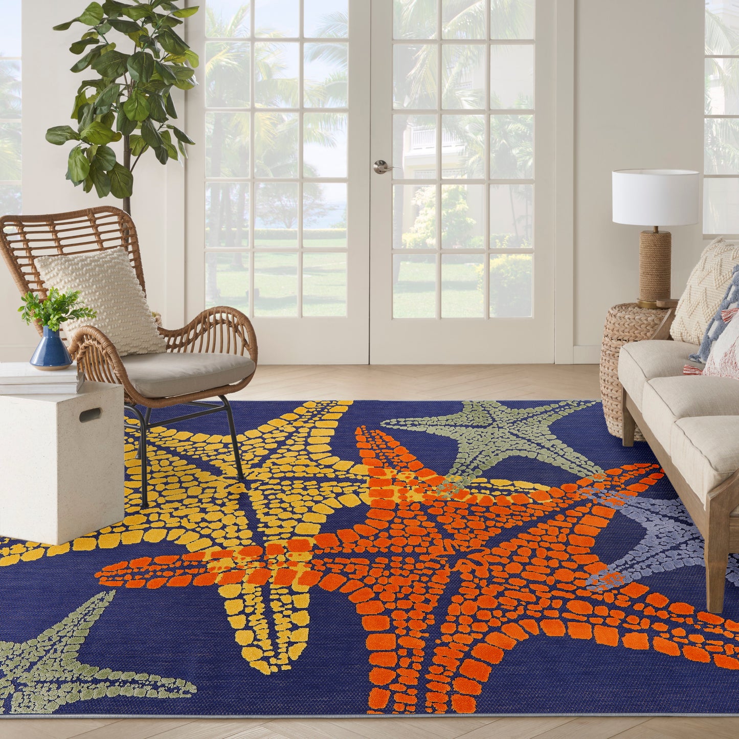 Outdoor navy rug with orange, yellow and green starfish; wicker chair, cream sofa, and potted plant.