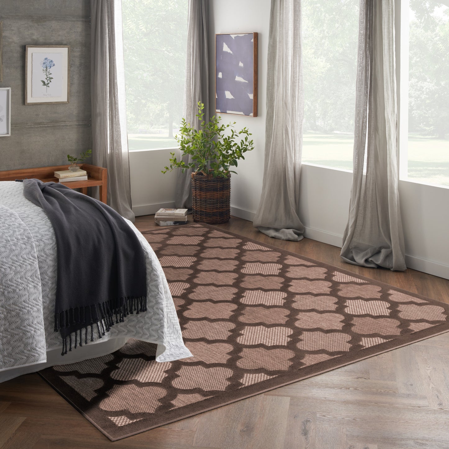 Brown area rug with beige lattice pattern in a modern rustic bedroom; beside bed with gray throw, windows, potted plant.