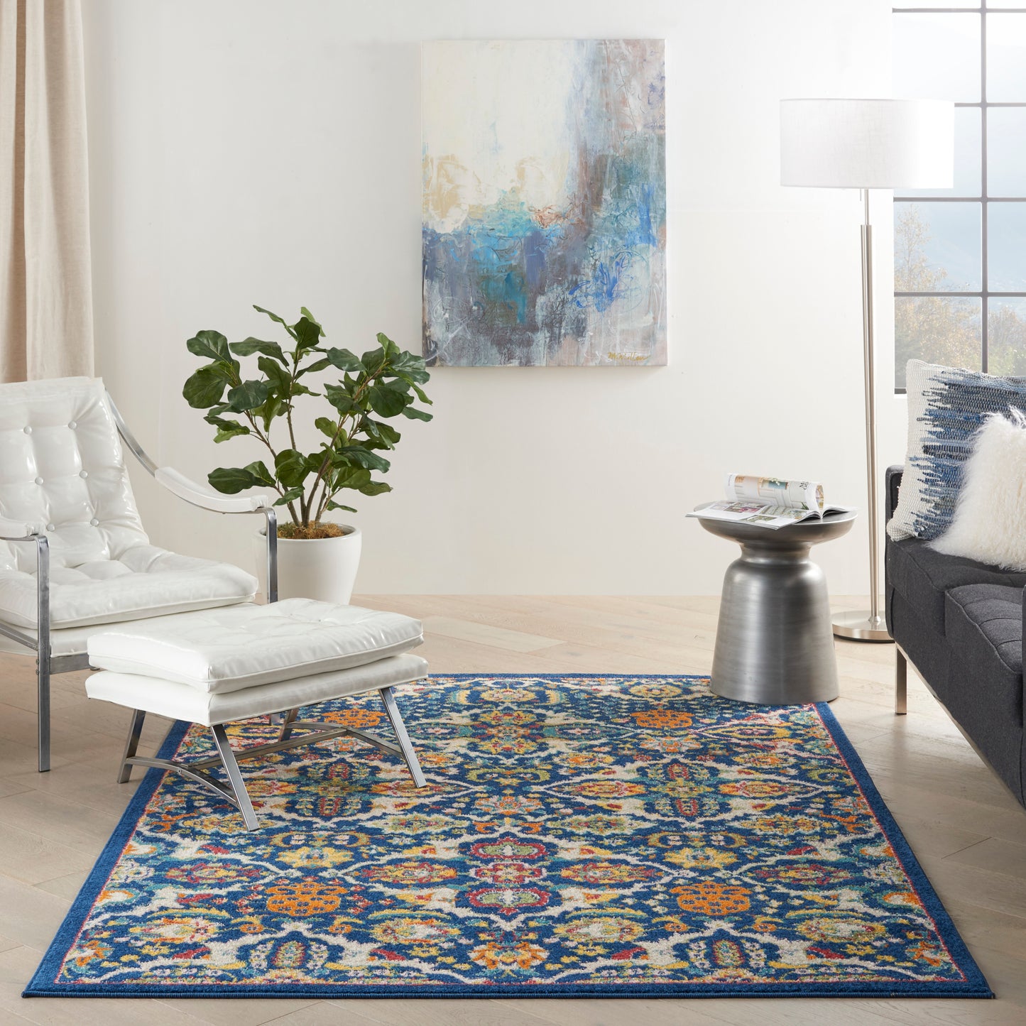 Blue multicolor area rug with orange and yellow accents in a modern living room with white lounge chair, plant, and wall art.