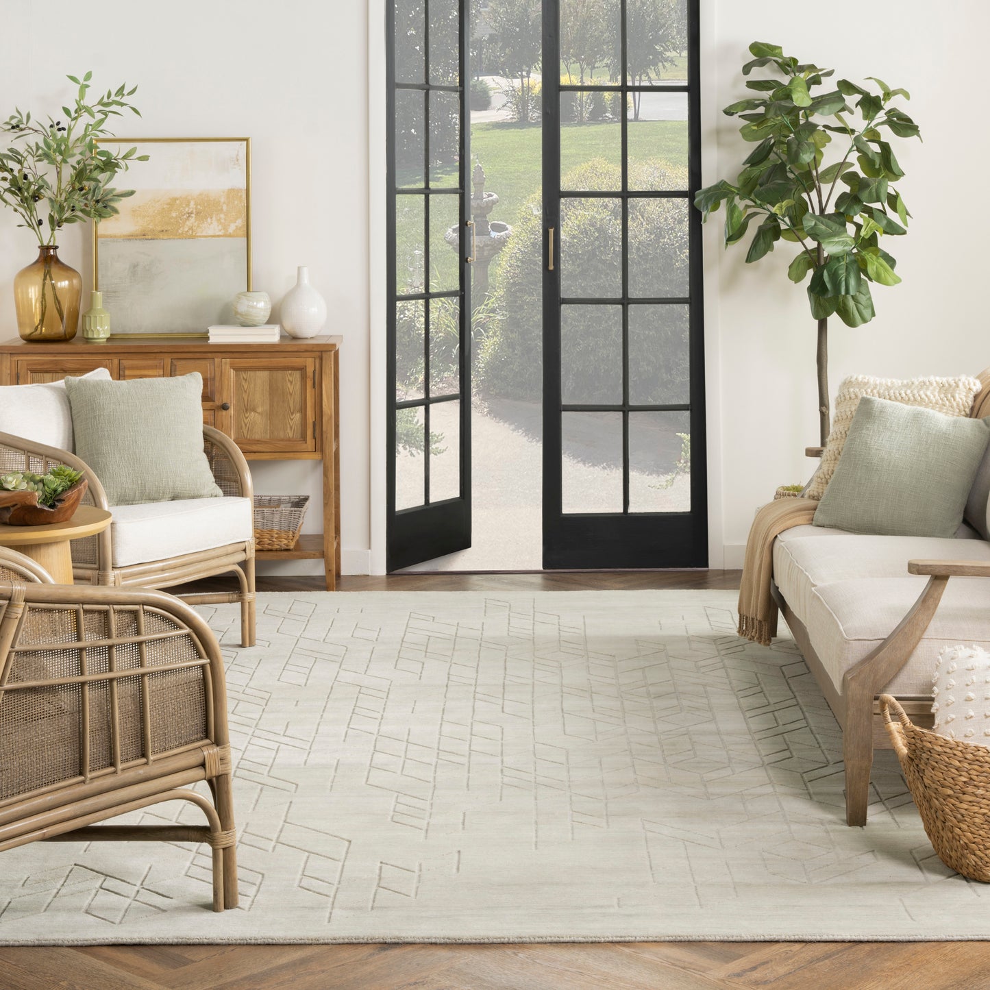 Bright living room with black framed glass doors, rattan furniture, cream sofa, and a light geometric rug.