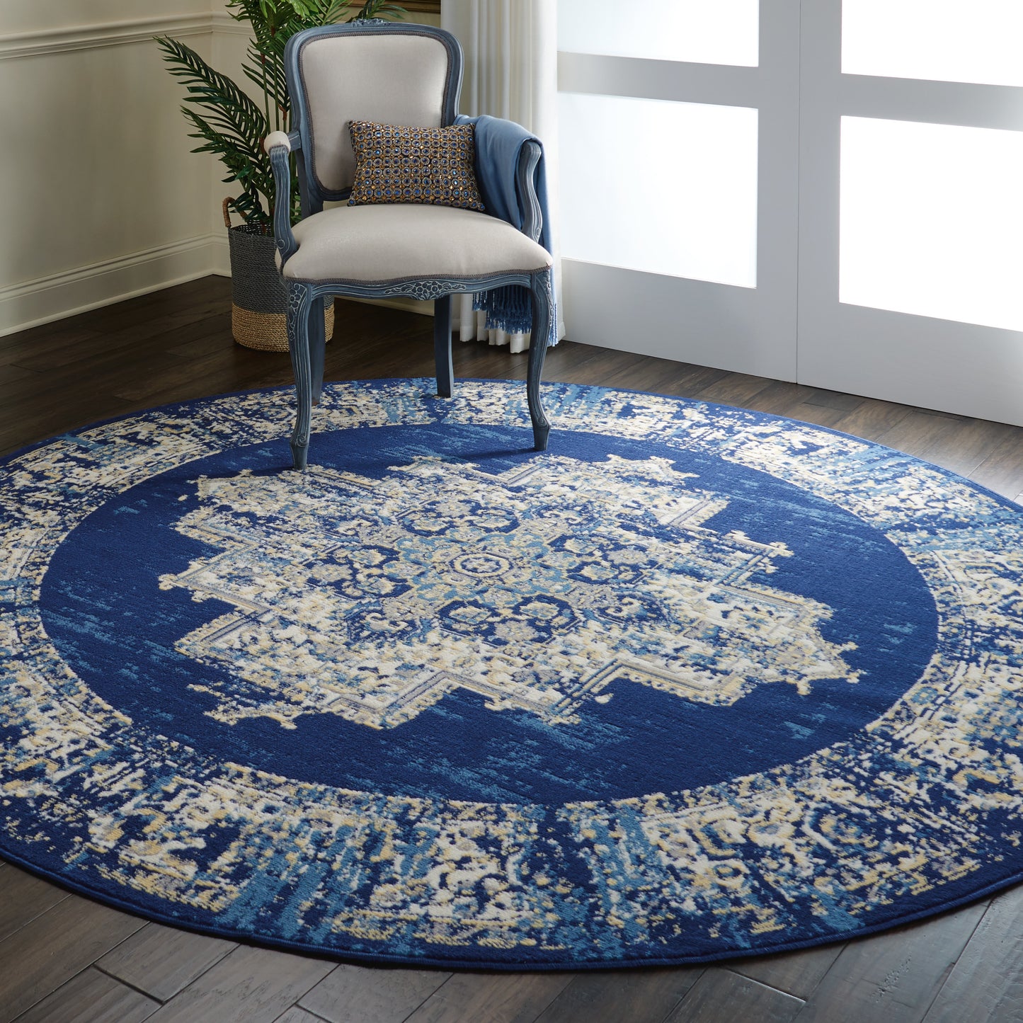 Circular navy and ivory oriental rug with medallion under a blue-gray carved armchair and blue throw.