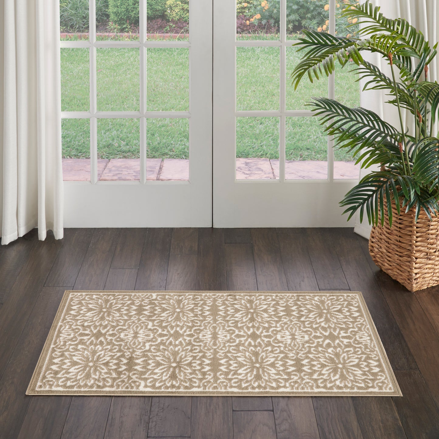Beige damask-patterned rectangular rug on dark wood floor by French doors; tall potted palm in wicker basket to the side.
