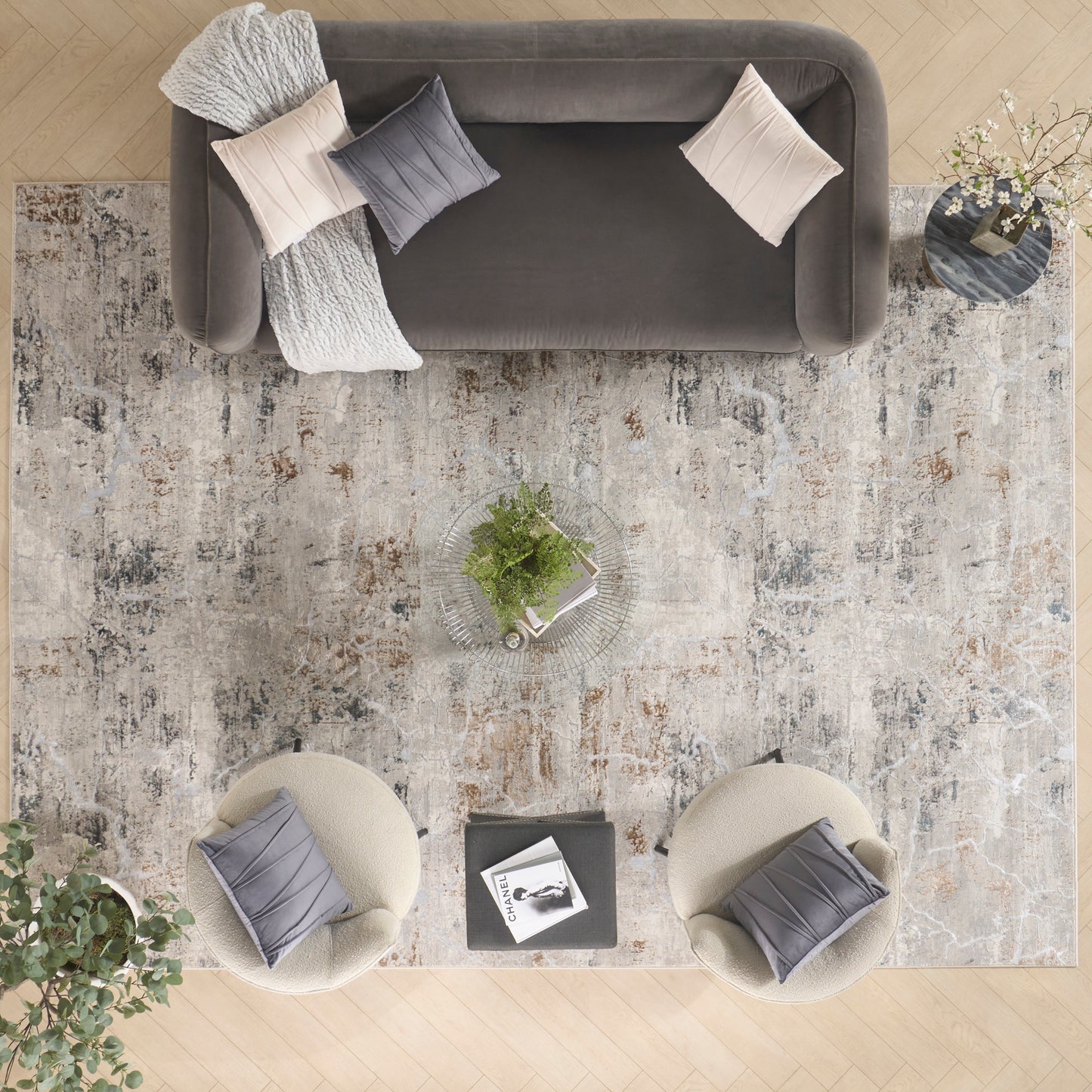 Overhead view of a gray sofa, two cream boucle chairs, a gray rug, glass coffee table with plants, and neutral cushions.