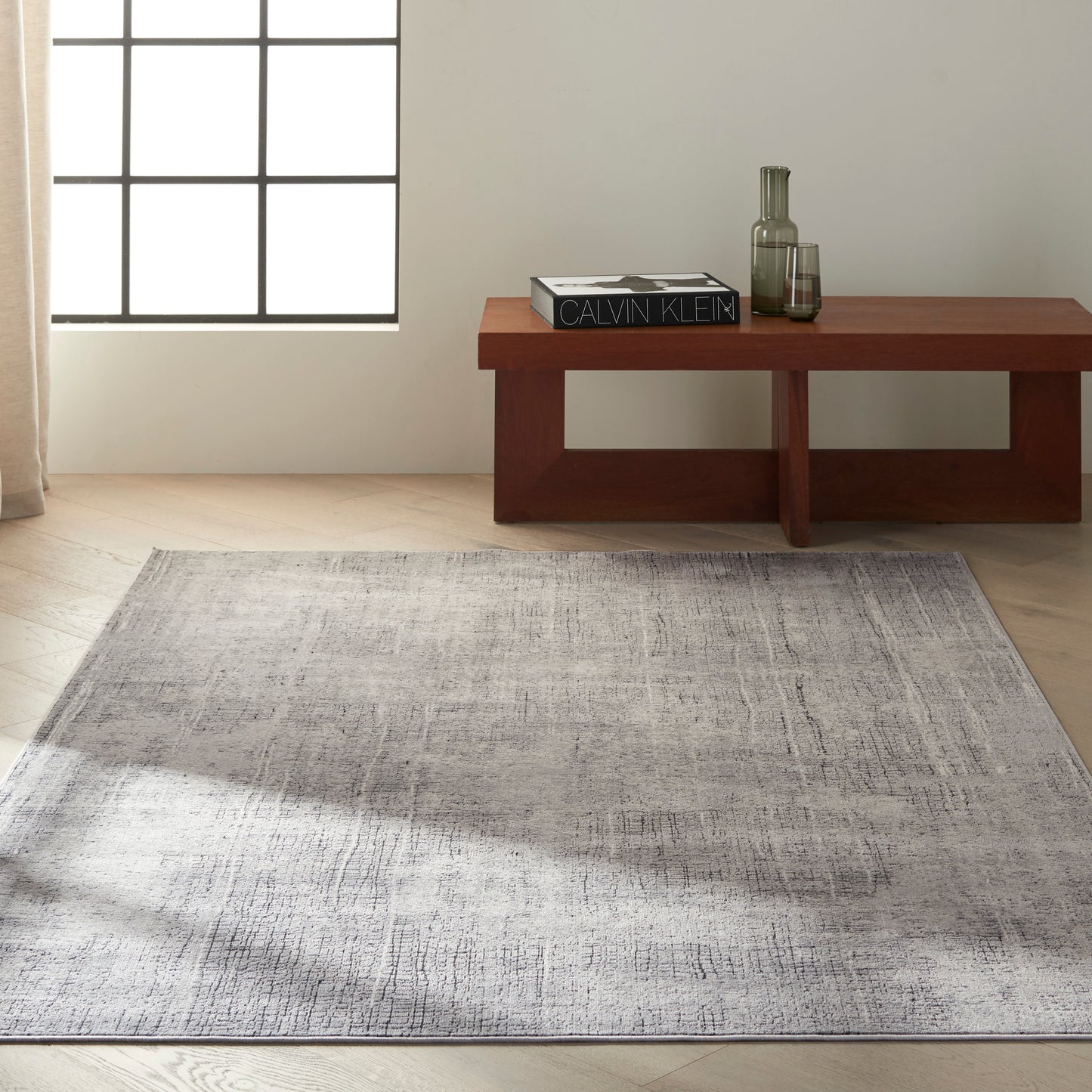 Minimalist living room: low rectangular wooden coffee table with a C K Design book and glassware, atop a grey textured rug.