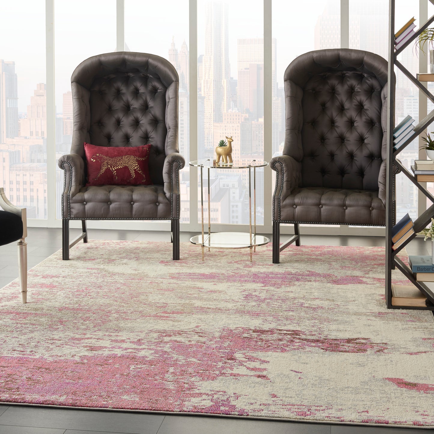 Two dark brown tufted leather high-back chairs with nailhead trim, glass side table, pink-beige abstract rug, city skyline.