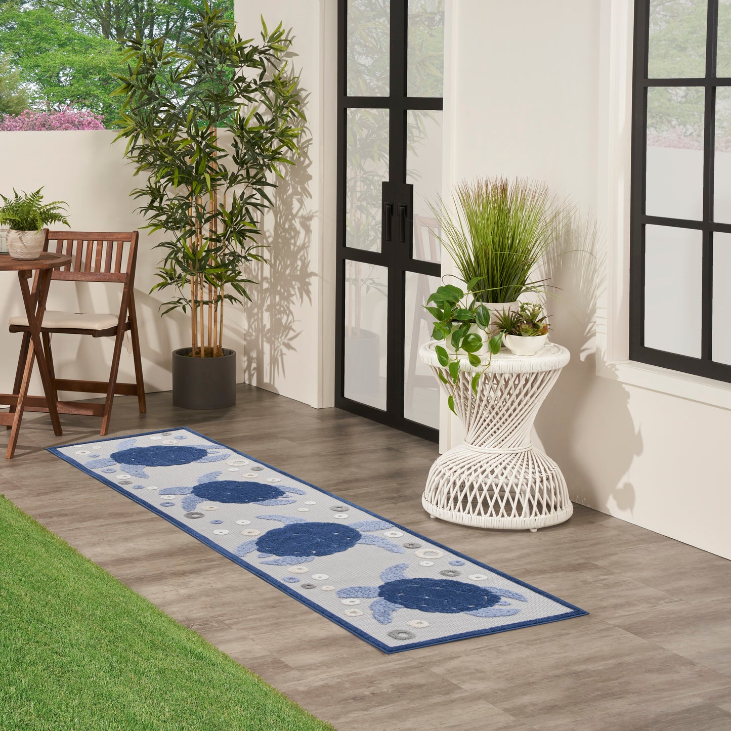 Outdoor runner rug with blue circular motifs on a gray field and blue border, laid on a wood deck beside glass doors.