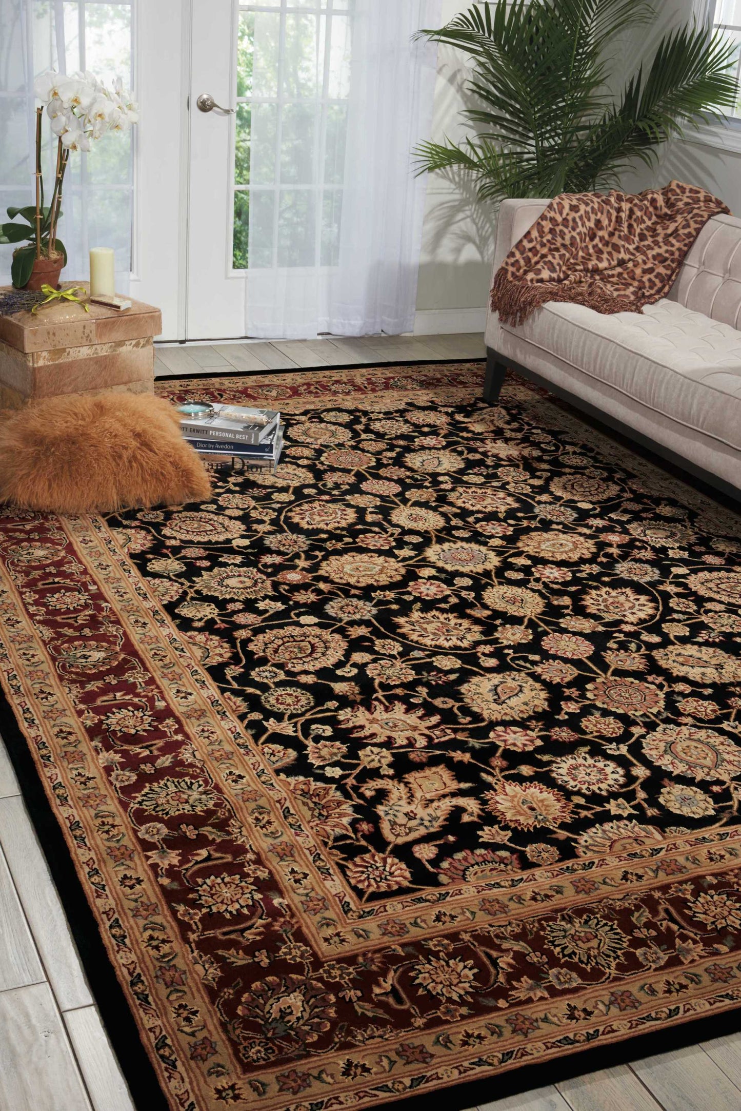 Large Persian-style rug with black field, gold floral motifs & red border in a bright living room.