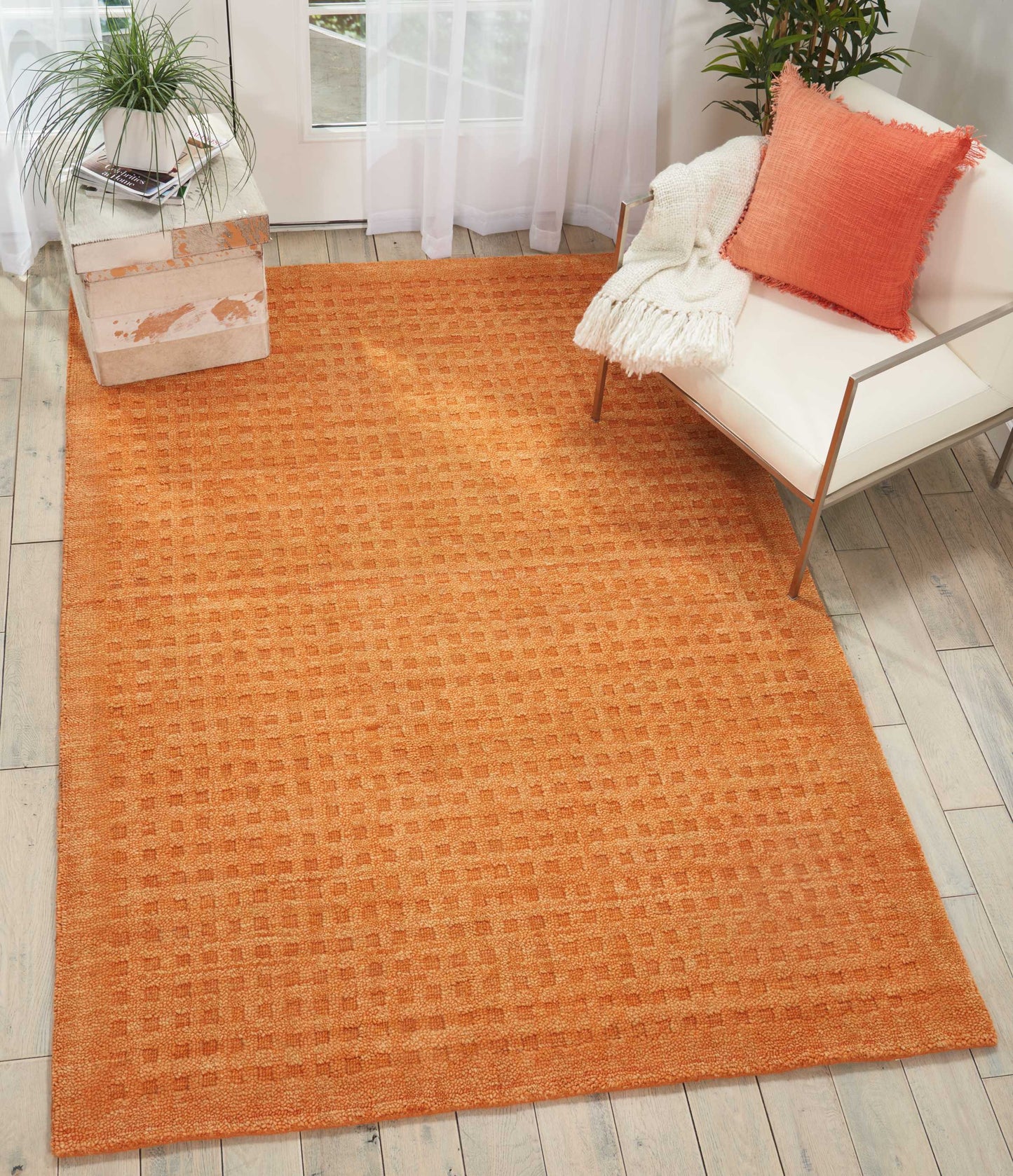 Orange textured area rug with subtle square pattern in a bright living room beside a white sofa and potted plant.
