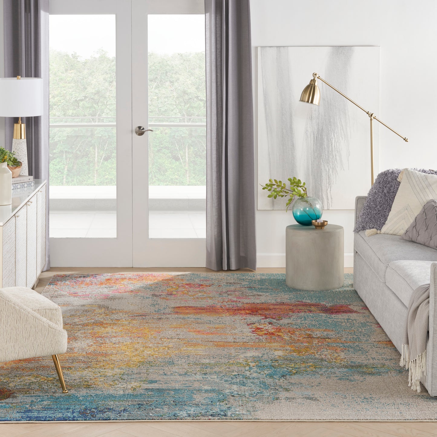 Modern living room with colorful rug, gray sofa, glass doors, gold arc floor lamp, concrete side table, turquoise vase.
