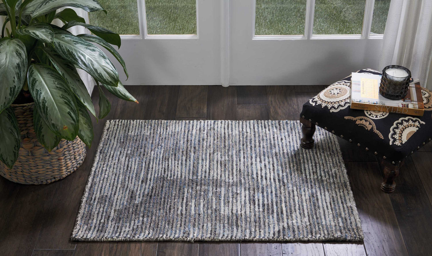Grey striped low-pile area rug on dark wood floor with potted plant and ornate black-and-gold coffee table near glass doors.