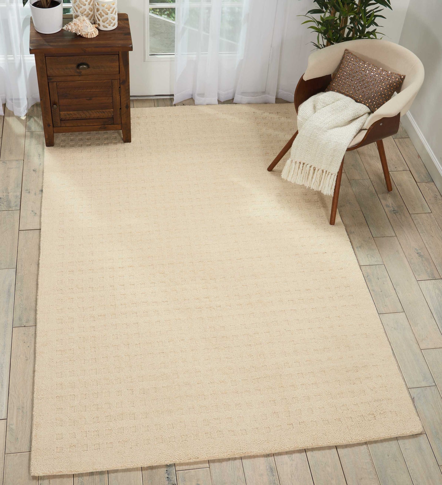 Beige woven area rug on light wood floor; mid-century chair with cream throw and wooden side table.